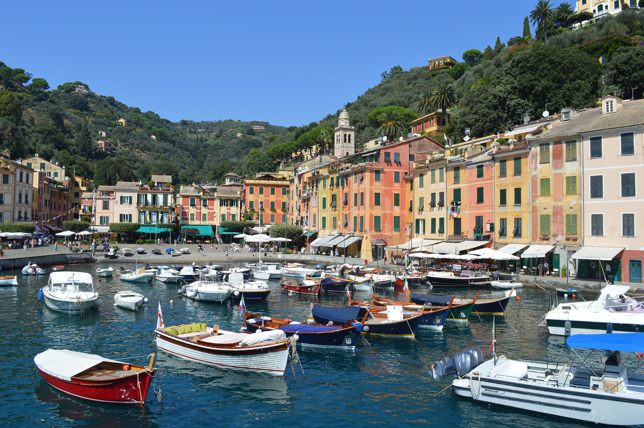 Small harbour with colourful buildings by the edge, hills behind, small boats in the water