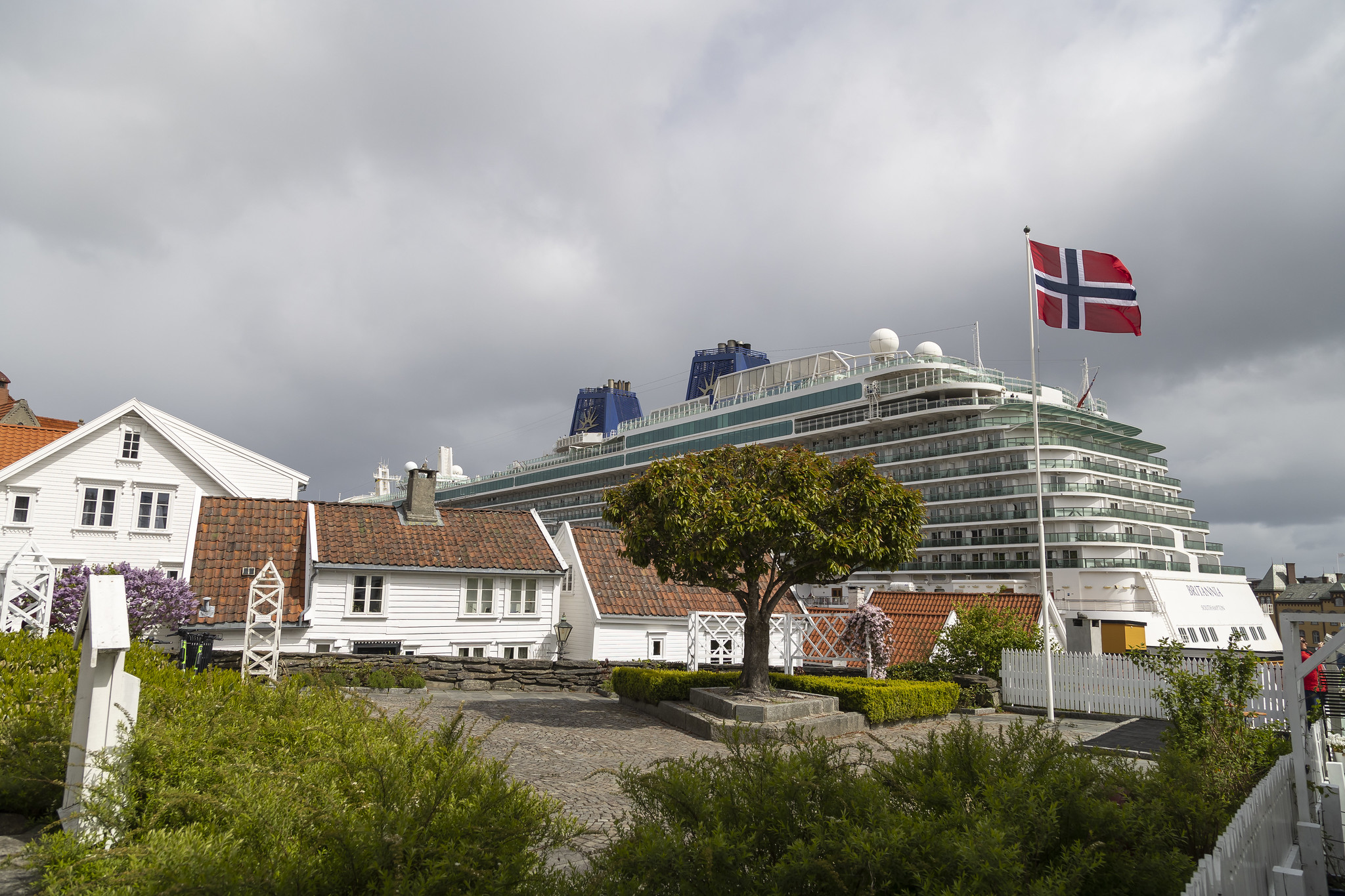 Cruise ship docked behind an old town area of white buildings and a Norewgian flag.