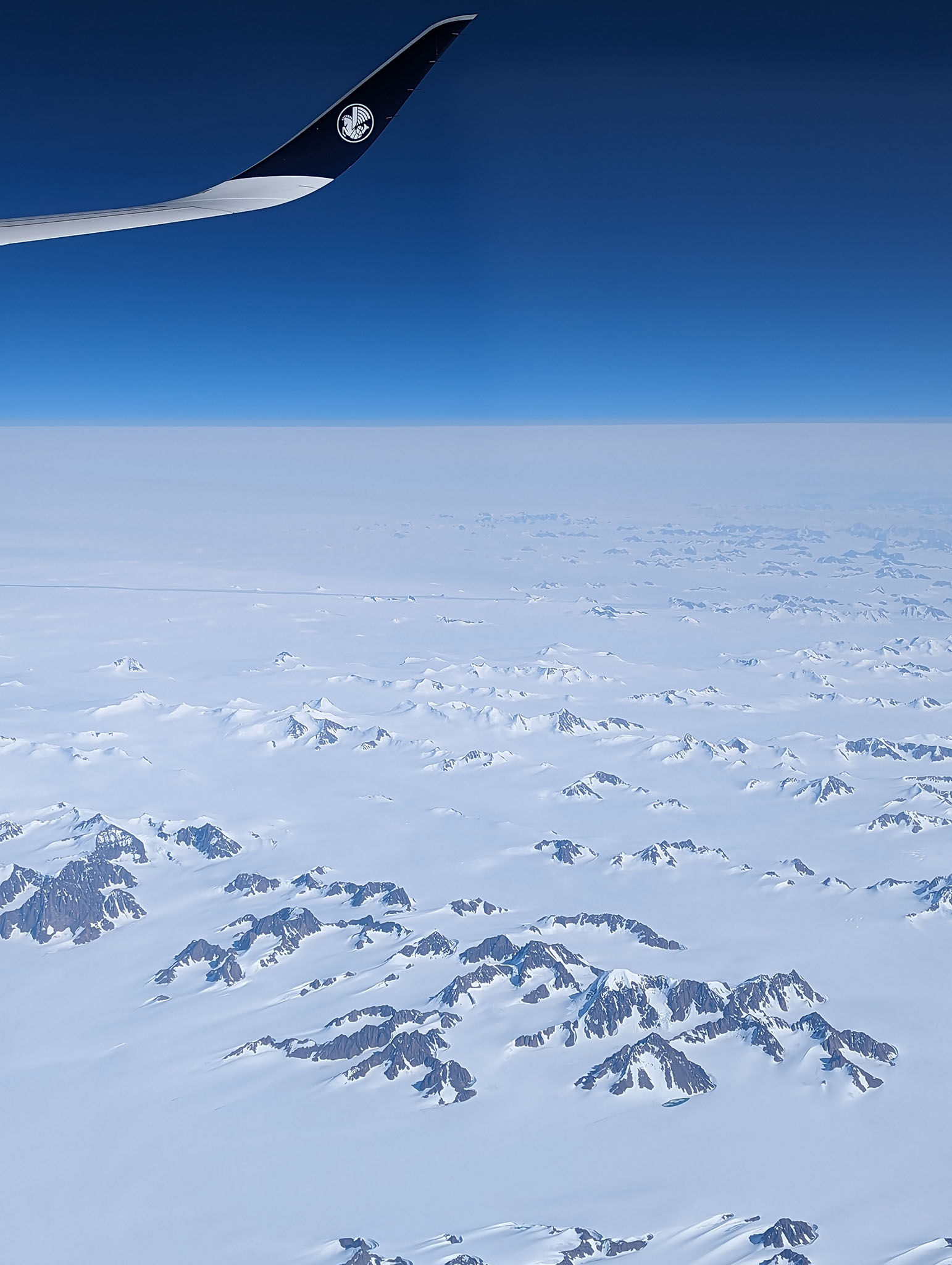 View from airplane over white, icy landscape and vibrant blue sky.